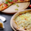 Dwie włoskie pizze na drewnianych talerzach, w towarzystwie pomidorków koktajlowych i parmezanu