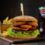 Hamburger z krążkami cebuli, bekonem i soczystą sałatą, z frytkami i szklanką coli w tle